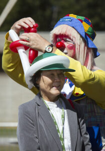 A clown making a balloon hat for a woman during a tailgate.