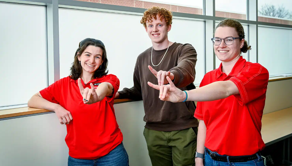 Three of NC State's Student Mental Health Ambassadors pose for a photo with wolfies up. From the left, they are: Alexis Jacobs, Caleb Moore, and Lauren Bradley.